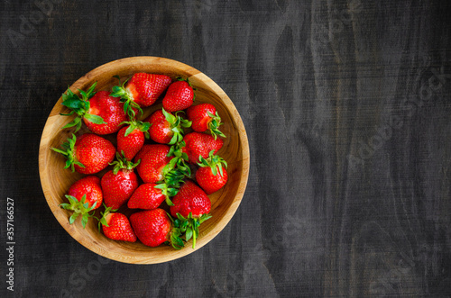 Fresh strawberries in a wooden bowl on a dark wooden background. Horizontal, copy space.