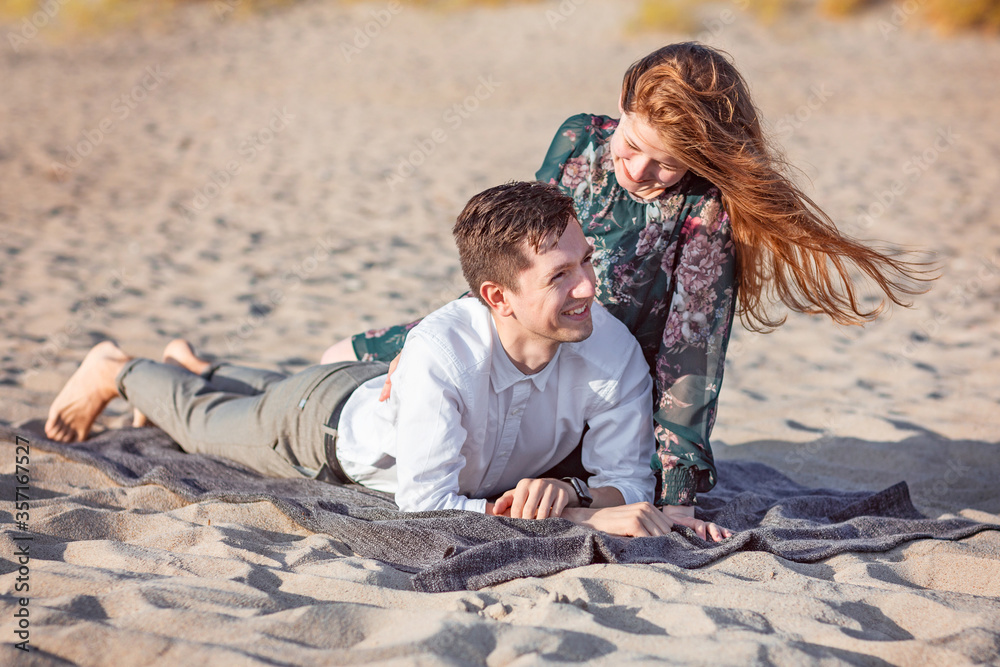 Young couple relax in the sand in clothes on the seashore, talk and laugh. Love, trust, always be together concept Young couple relax in the sand in clothes on the seashore, talk and laugh. Love, trust, always be together concept