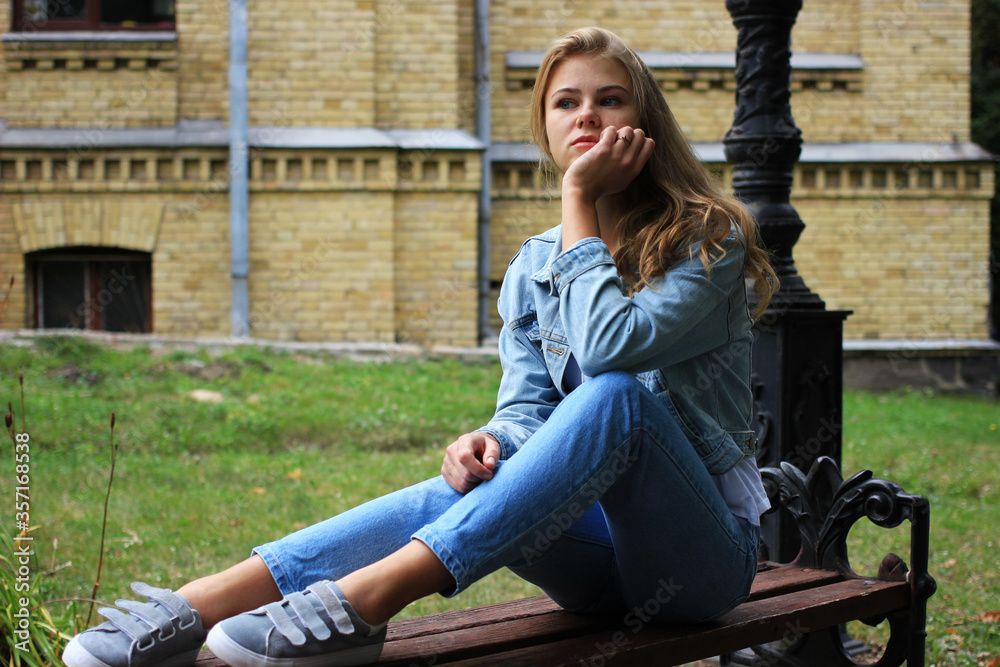 A pensive and sad, beautiful blonde student girl sits on a bench. A pensive and sad, beautiful blonde student girl sits on a bench.