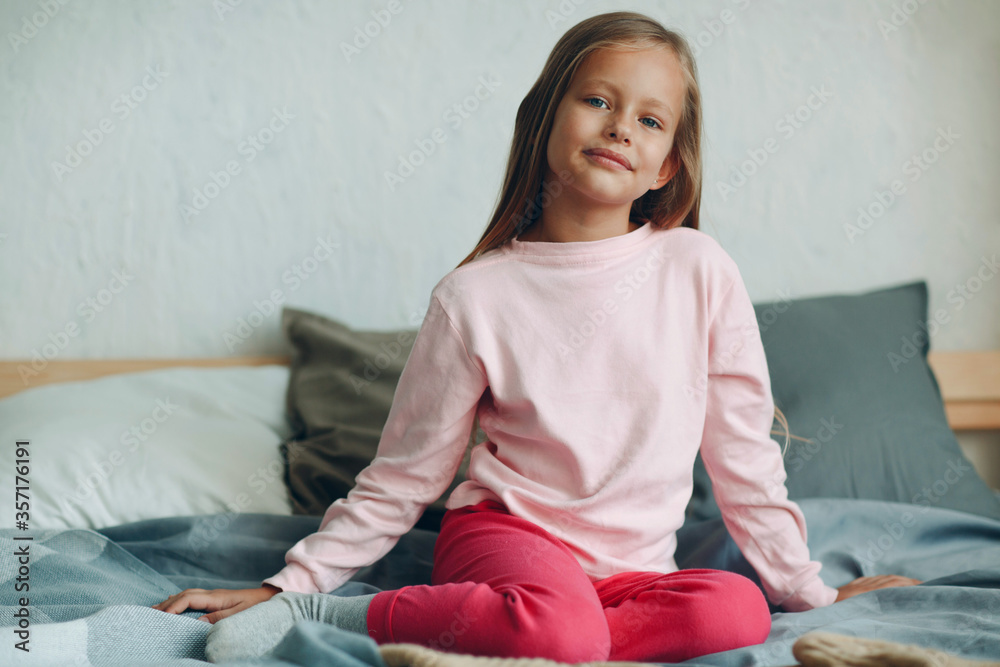 Smiling portrait of little girl sitting on bed. Stock Photo | Adobe Stock