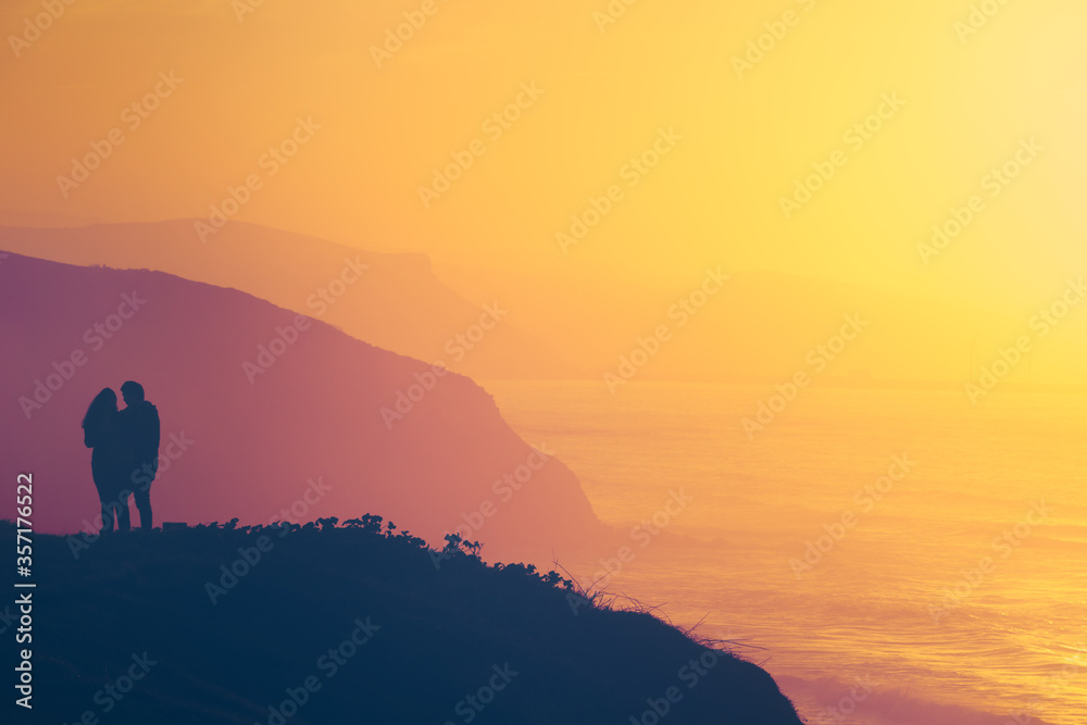 romantic scene of a couple on cliff watching the sea