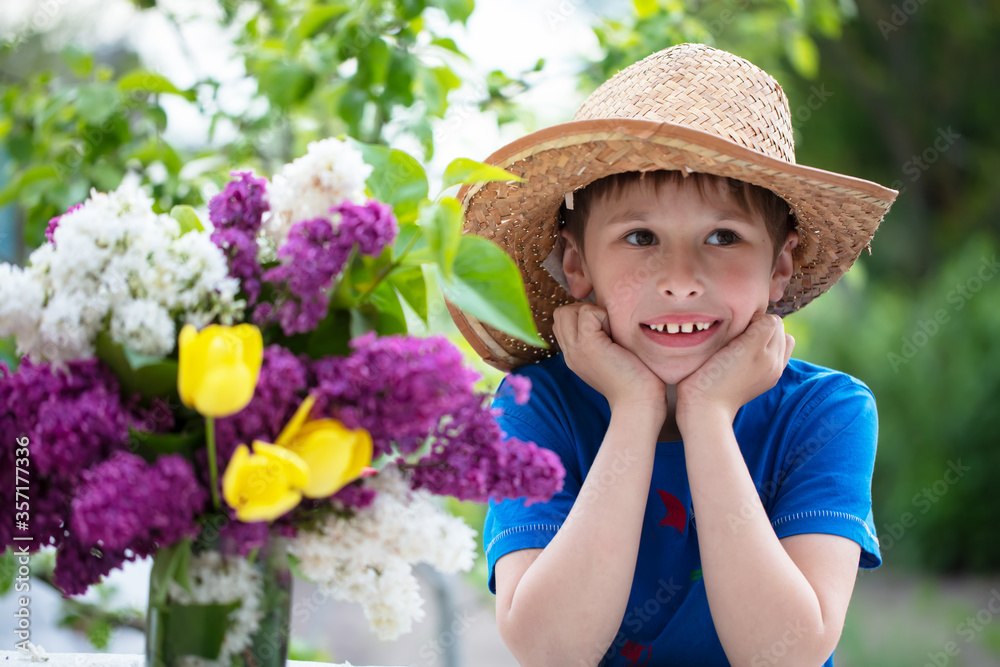 Fototapeta premium Funny child in panama with a bouquet of flowers. Happy boy in the summer.