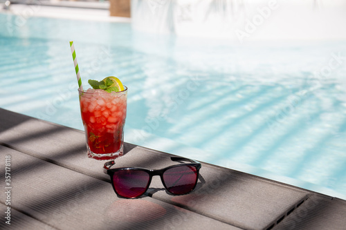 fresh red cocktail near sunglasses and swimming pool in summer