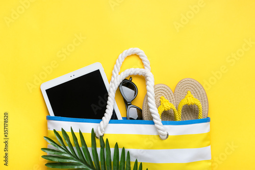 Fototapeta Naklejka Na Ścianę i Meble -  Swimming accessories - trendy beach bag with stripes, black glasses, white tablet, palm leaf, yellow flip flop on yellow background Flat lay Top view Summer, travel, vacation concept 