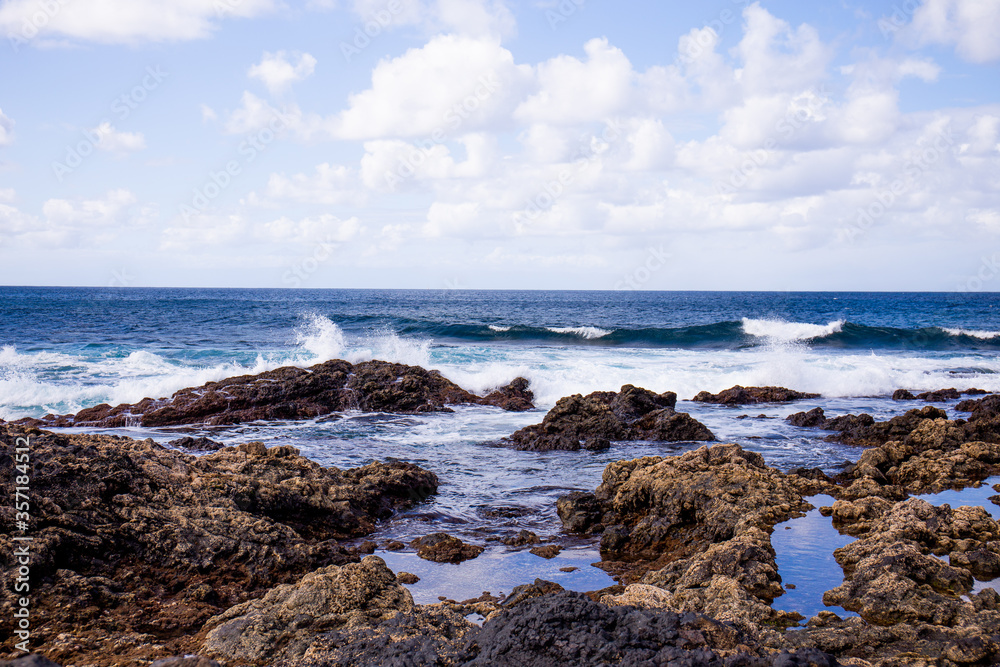 Atlantic ocean with waves and rocks against blue sky with clouds in Agaete, Las Palmas