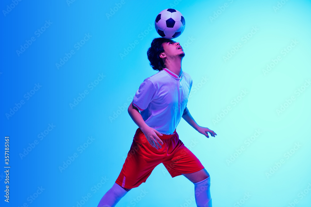 Passioned for game. Football or soccer player on gradient blue studio background in neon light - motion, action, activity. Concept of sport, competition, winning, action, motion, overcoming. Copyspace