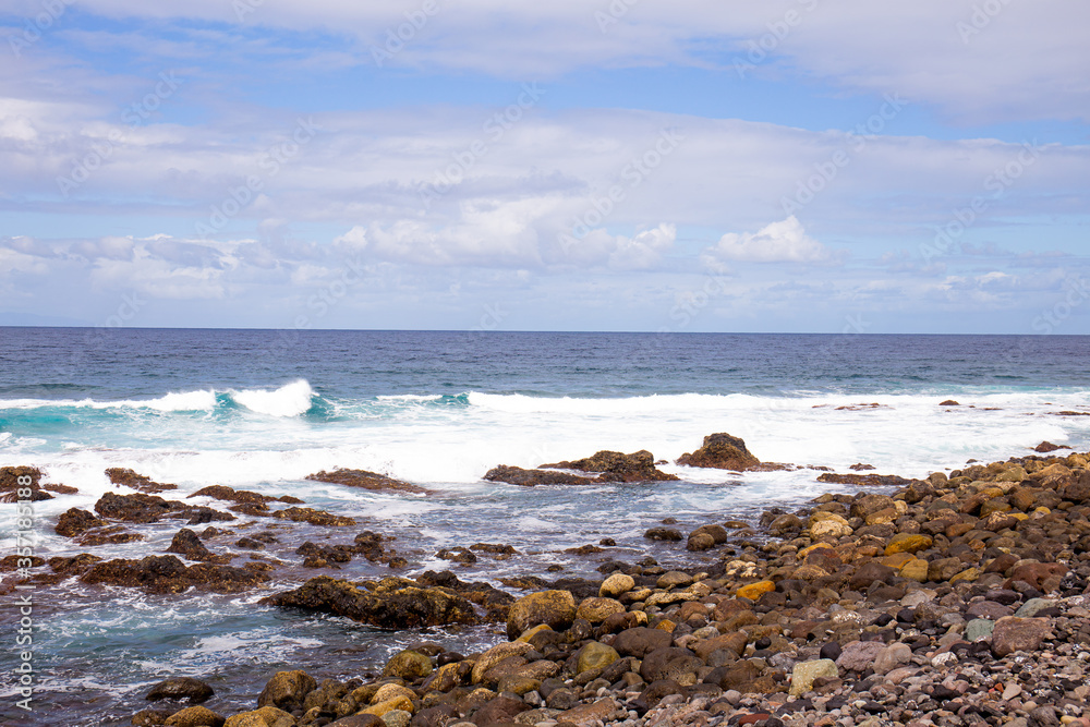 Atlantic ocean with waves and rocks against blue sky with clouds in Agaete, Las Palmas