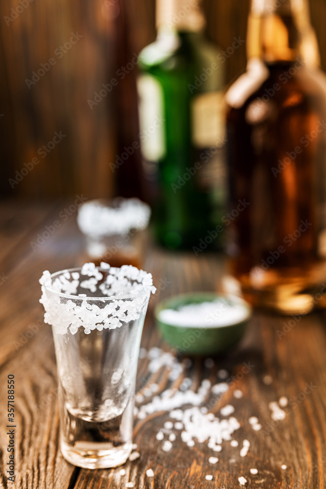 An empty tequila glass, with salt at the edges, stands on the bar, in the background are different bottles of alcohol, shallow depth of field, selective focus. The concept of a drink in the bar.