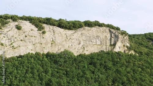 Large aerial zoom of a climber on a huge limestone cliff with a forest at the bottom