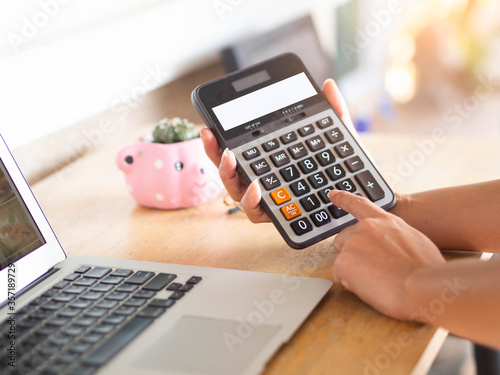 Hand with calculator on table with laptop in home.