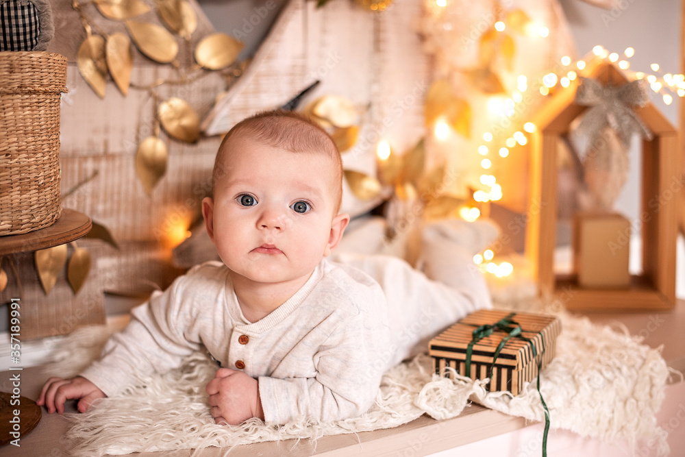 A small baby in light clothing lies on the background of the Christmas decor. A small baby in light clothing lies on the background of the Christmas decor.