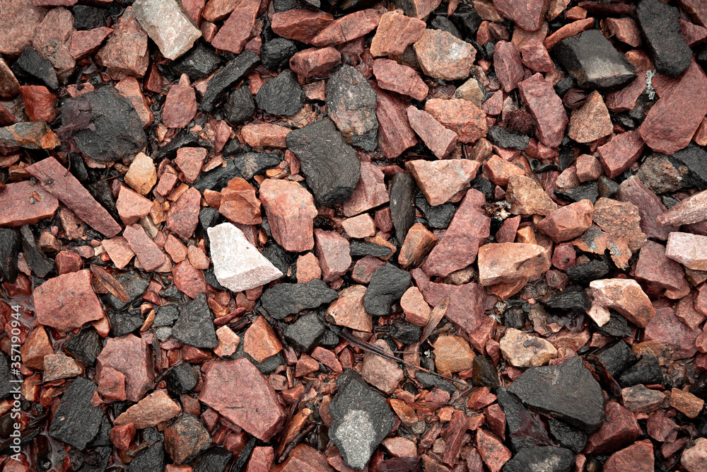 A closeup of wet textured rocks and stones of red, brown, orange and grey color A closeup of wet textured rocks and stones of red, brown, orange and grey color