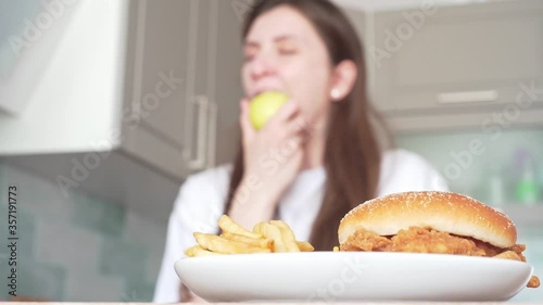 Vegan woman eats an apple against the backdrop of unhealthy fast food. Choosing the right food