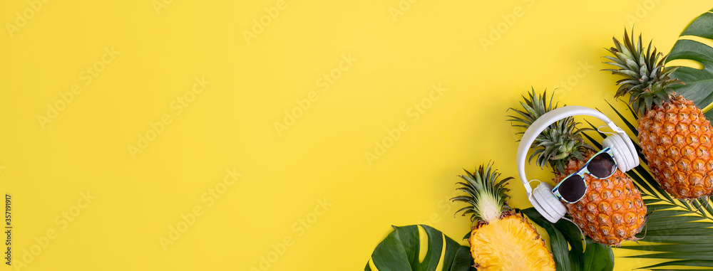 Funny pineapple wearing white headphone, listen music, isolated on yellow background with tropical palm leaves, top view, flat lay design concept. - obrazy, fototapety, plakaty 