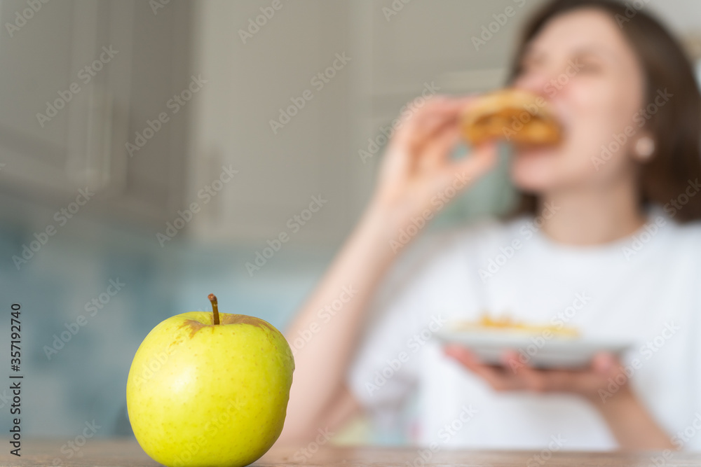 Unhealthy food choices. Wrong nutrition and overeating. Woman eats cheeseburger and fries against apple Unhealthy food choices. Wrong nutrition and overeating. Woman eats cheeseburger and fries against apple