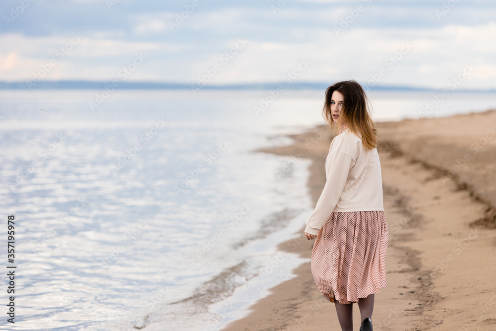A young beautiful girl walks along the shore and looks back.