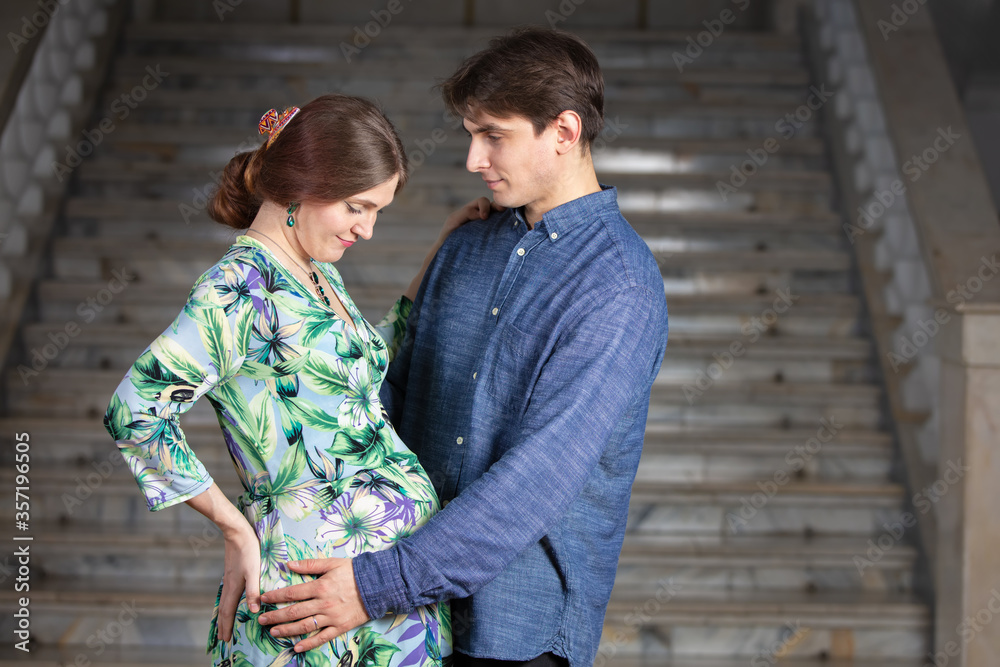 Pregnant woman with husband on gray background.