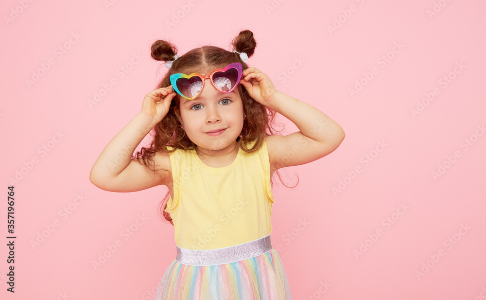 Portrait of surprised cute little toddler girl  in sunglasses over pink background.  Child model have fun and jump. Advertising childrens products - obrazy, fototapety, plakaty 