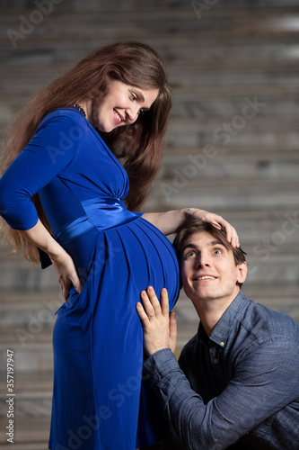 Handsome man listens to tummy of his beautiful pregnant wife and smiles