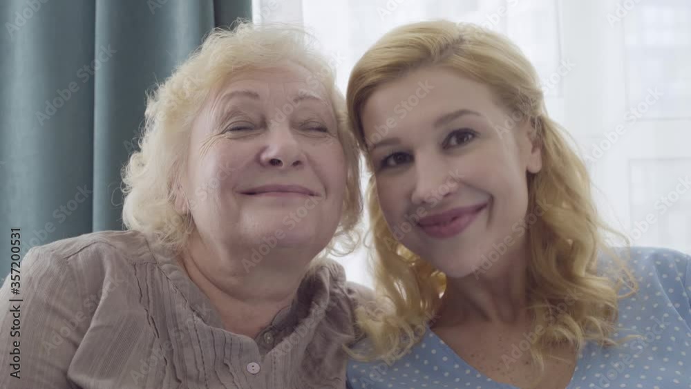 Attractive woman kissing mother's cheek, looking at camera, unconditional love Attractive woman kissing mother's cheek, looking at camera, unconditional love
