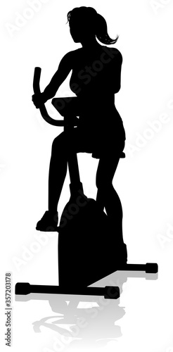 A woman in silhouette using a stationary exercise spin bike piece of gym equipment fitness machine