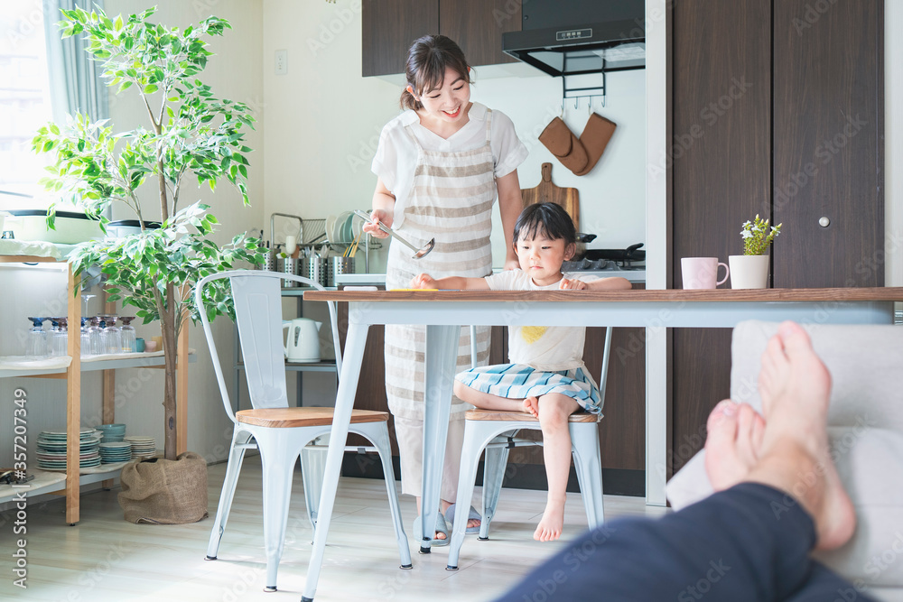 キッチンでお絵かきをする女の子と、料理をしながら見守る母親