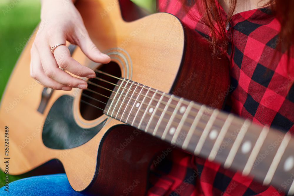Fototapeta premium close-up of a brown classical acoustic guitar with the hand of a female musician playing the strings. Stringed musical instrument in the hands of a person close up on a blurred natural background