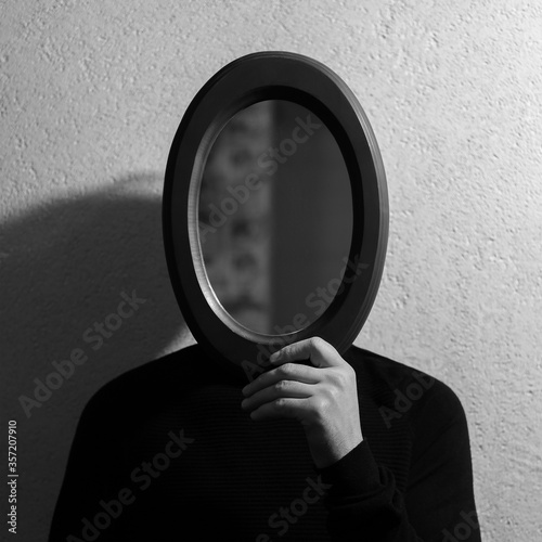 Foto Black and white studio portrait of young man holding oval mirror on face