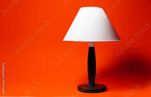 Close-up of night lamp with white shade and black tripod on background of lush lava color.