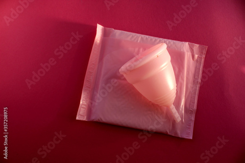 Fototapeta Naklejka Na Ścianę i Meble -  A pink menstrual Cup rests on a Packed pad