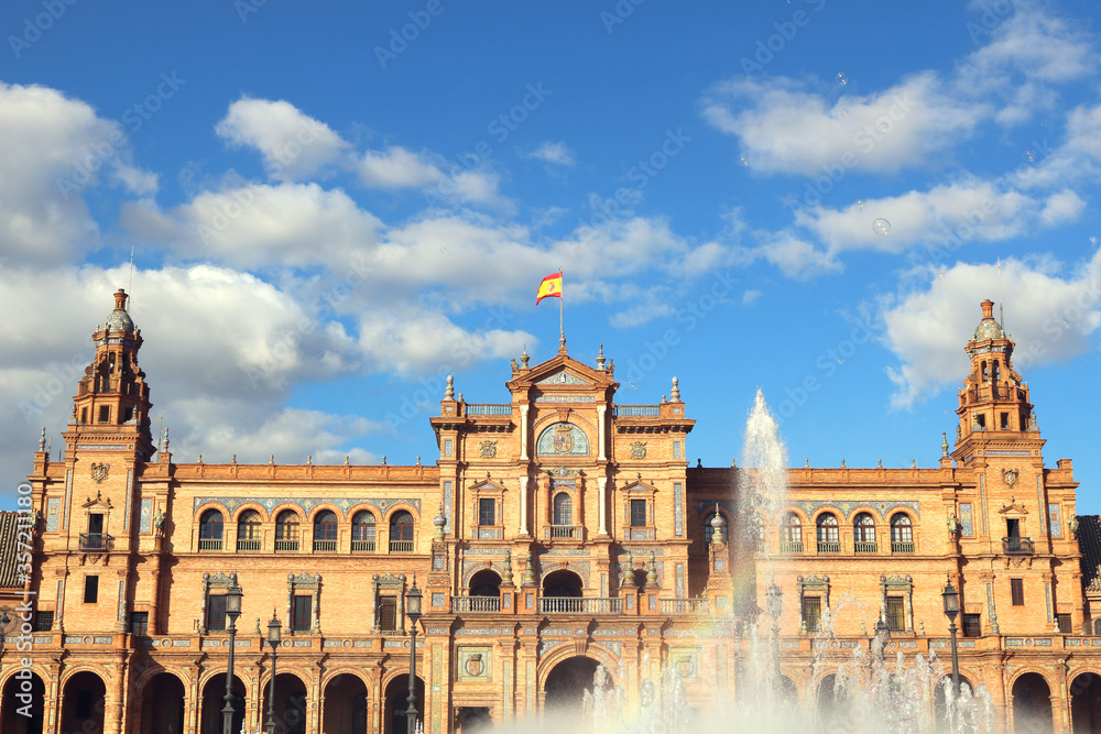 plaza de espana seville spain, with the main monument palace, the flag, the fountain and a blue sky with clouds in the background - horizontal postcard or wallpaper