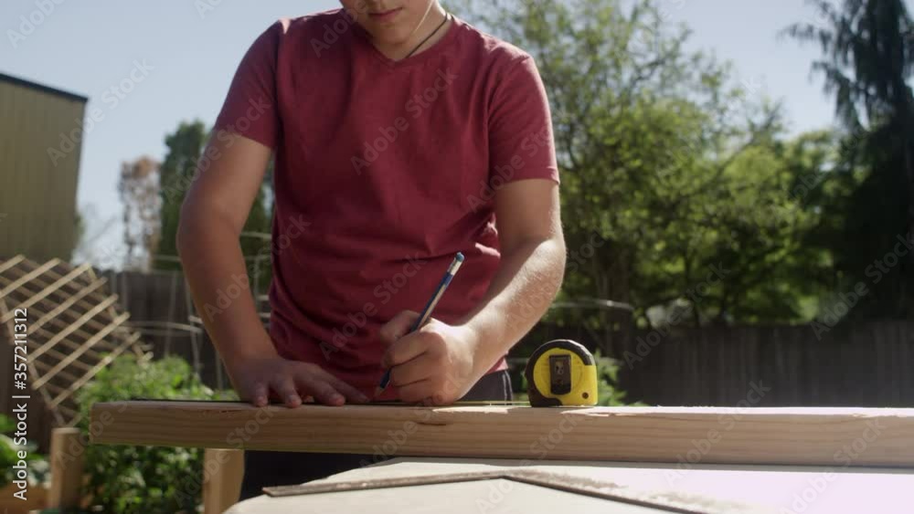 Pan up to a young teenage boy using a tape measure while working on a backyard DIY project Pan up to a young teenage boy using a tape measure while working on a backyard DIY project