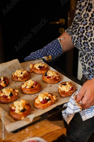 woman is holding a baking tray with freshly baked buns with fruits and crumble. homemade sweets, selective focus
