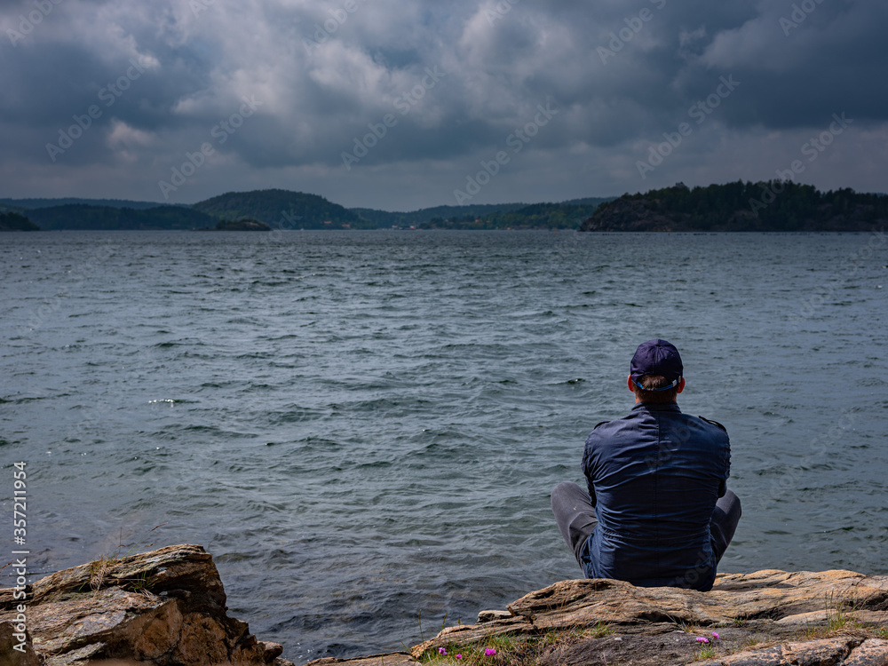 Social distancing, man sitting with back to the camera watching the ocean