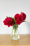 Bright red peonies in a beautiful glass jug on a wooden table