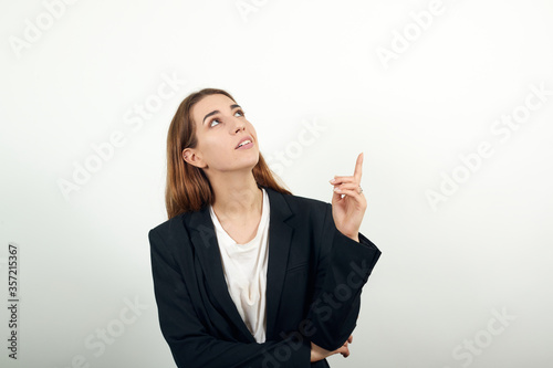 Hand pointer with forefinger pointing up. Index finger to show direction. Means choosing, introducing too. Indicating towards. Young attractive woman with brown hair in light t-shirt, black jacket © Petro