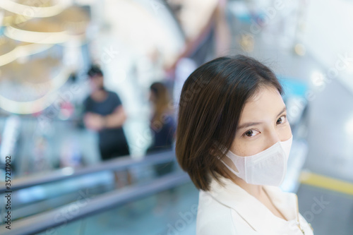 Woman wearing face mask at shopping mall on escalator for protection coronavirus.