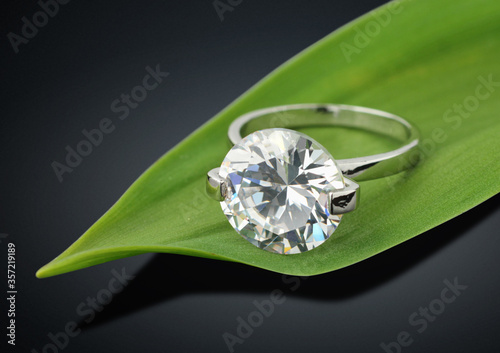 Jewelry ring with big diamond on green leafs background