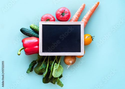 Small blackboard with vegetables around. Healthy concept on blue background with copy space