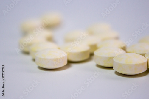 Close up of pale yellow disk-shaped medical tablets (pills) on white background.
