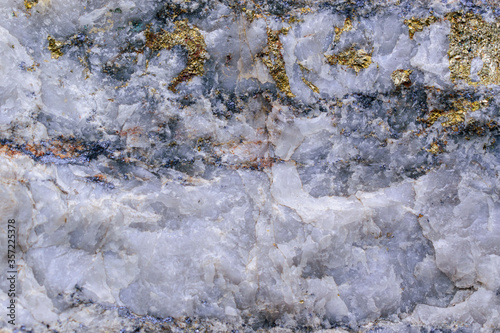 Streaks and inclusions of molybdenum ore in granite stone. Massive sulfide ore. Glitter of steel and gold. Minerals - molybdenite, pyrite, chalcopyrite, white quartz. Concept of mining useful metal.