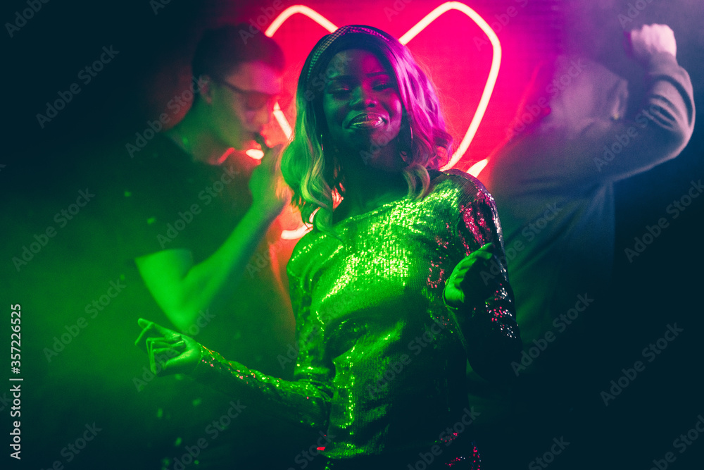 Sexy African American woman dancing in bright colors of neon lighting of night club. Young woman and crowd of people having fun at night disco.