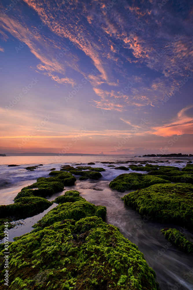 Fototapeta Beautiful sunrise in rocky beach covered by green moss with colorful cloud on sky in Sawarna, Banten, Indonesia