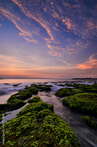 Beautiful sunrise in rocky beach covered by green moss with colorful cloud on sky in Sawarna, Banten, Indonesia