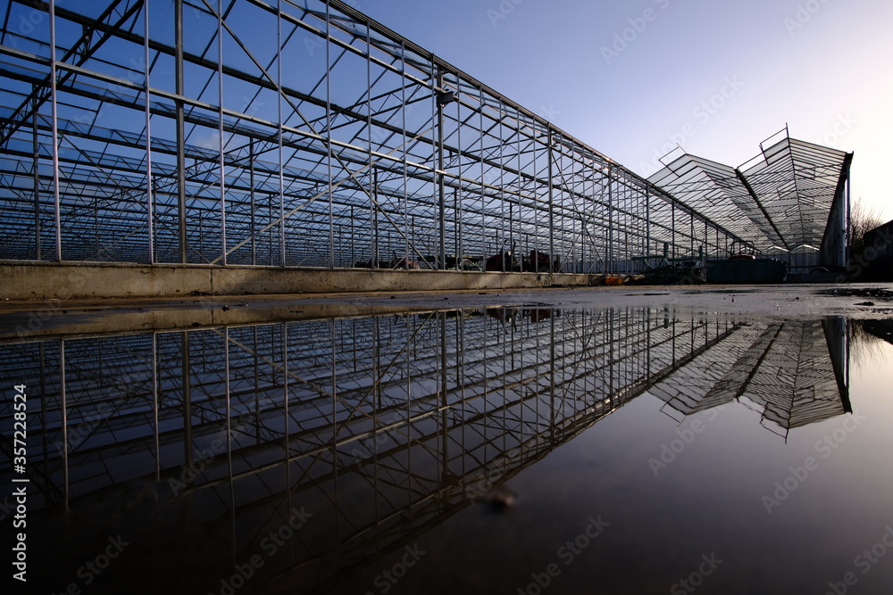 Fototapeta premium Structural steel structure of a greenhouse with reflection against a clear blue sky in the background