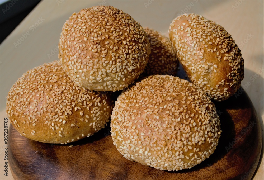 Rye homemade buns with sesame seeds on a flat wooden plate Rye homemade buns with sesame seeds on a flat wooden plate