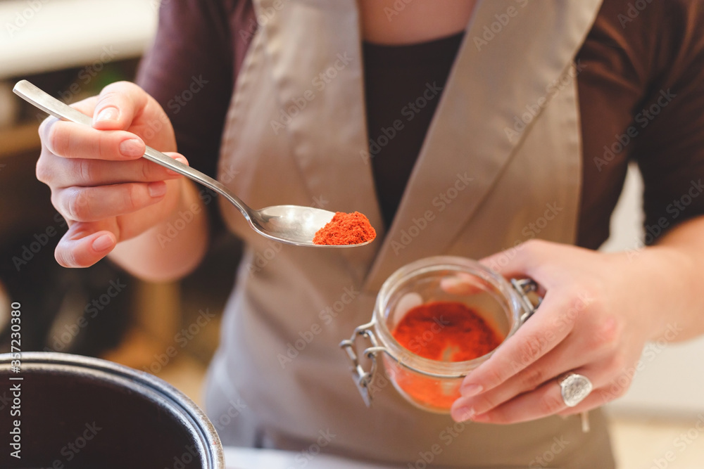 Female cook adds paprika spices while cooking tomato soup.Close-up view on spoon with red pepper.