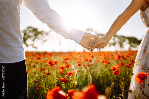 Holding hands of happy young couple having fun in poppy field. Love. Together. Beautiful sunset on a summer day. © maxbelchenko