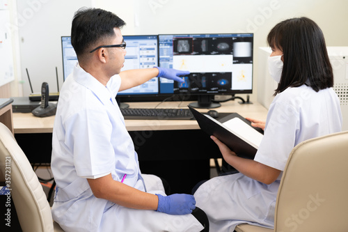 Asian radiologists shows the patient CT scan image at display for explaining treatment patient information to doctor in x-ray room.High technology for planing medical treatment equipment concept.