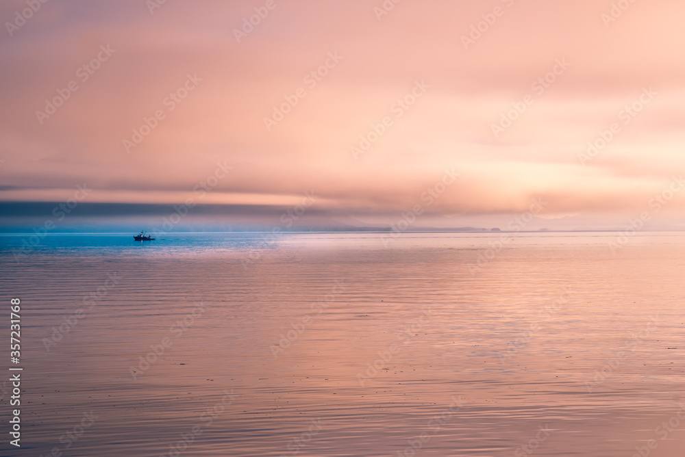 A sunset view of the coast of Alaska with a small fishing boat in the blue water
 


